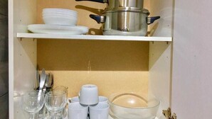 A kitchen with a pot, plates, cups, and a bowl on shelves. - En-suite Studio Room with Kitchenette, Parking (Greater London)