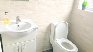 Ein Badezimmer mit einem weißen Waschbecken, einer Toilette und einem Fenster mit einer Pflanze.
