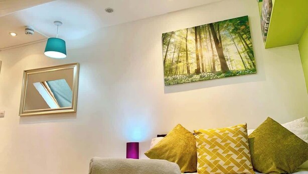 Ein Schlafzimmer mit einem Bett, einem Spiegel, einem Waldgemälde und einer türkisblauen Pendelleuchte.