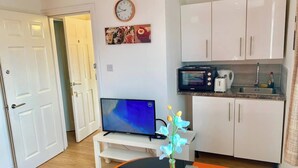 Ein kompakter Wohnraum mit Fernseher, einer kleinen Küchenzeile und einem Esstisch mit einer Vase.
