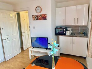 Een knus woongedeelte met een televisie, een kitchenette en een eettafel met een vaas.
