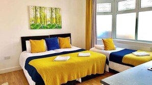 A hotel room with two beds, a painting on the wall, and a window with curtains.