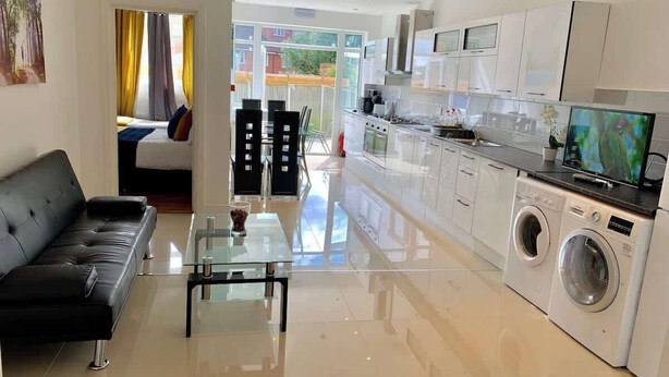 A modern kitchen with a washing machine, a dining area with a glass table, and a living room with a sofa.