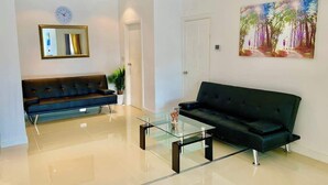 A modern living room with a glass coffee table, a black sofa, a painting on the wall, and a clock.