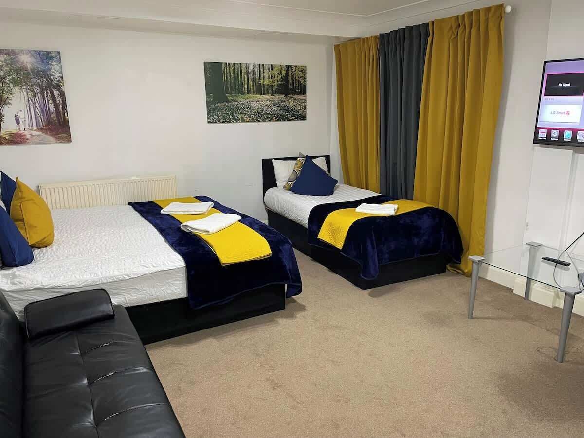 A hotel room with two beds, a sofa, a TV, and artwork on the walls.
