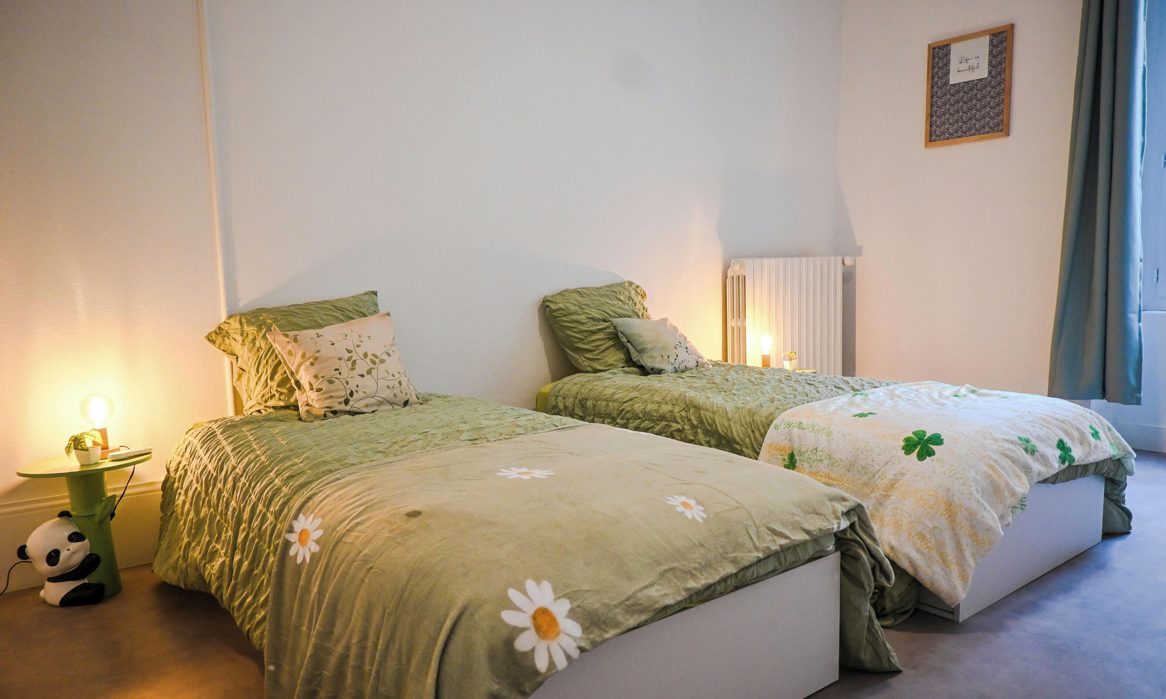 A bedroom with two beds, a bedside table with a lamp, a panda toy, and a framed picture on the wall.