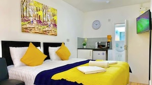 A bedroom with a bed, a painting, a clock, a TV, and a kitchenette. - Studio flat en-suite, Kitchenette, Parking, NP2 (Newbury Park)