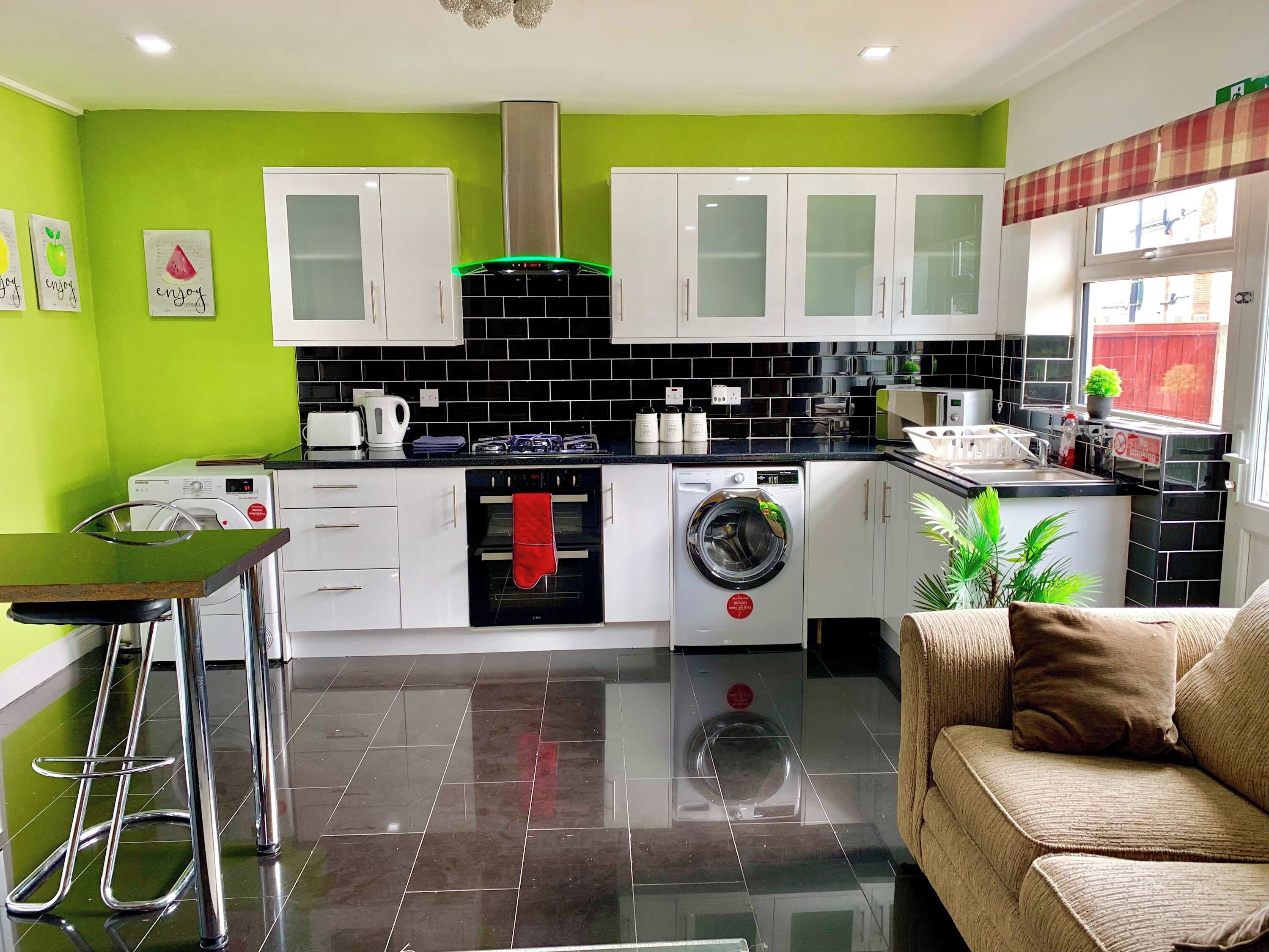 A compact kitchen with white cabinets, a black tiled backsplash, and a green wall.