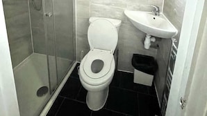 Un baño con ducha, inodoro, lavamanos y ventana.