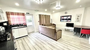 Una cocina moderna con encimera negra, sofá color beige, mesa de comedor con sillas rojas y televisor de pantalla plana montado en la pared.
