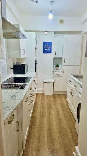 A modern kitchen with white cabinets, a built-in microwave, a stove, and a sink. - Cosy Stylish 2BR Garden Retreat, Pimlico Station (Greater London)