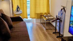 En kompakt opholdsstue med sofa, et lille bord, et fjernsyn og et tøjstativ.