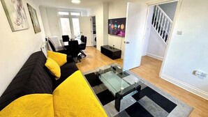 Een moderne woonkamer met een zwart-gele bank, een glazen salontafel en een trap naar een andere kamer.