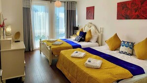 Een hotelkamer met twee bedden, een bureau en een groot raam met gordijnen.