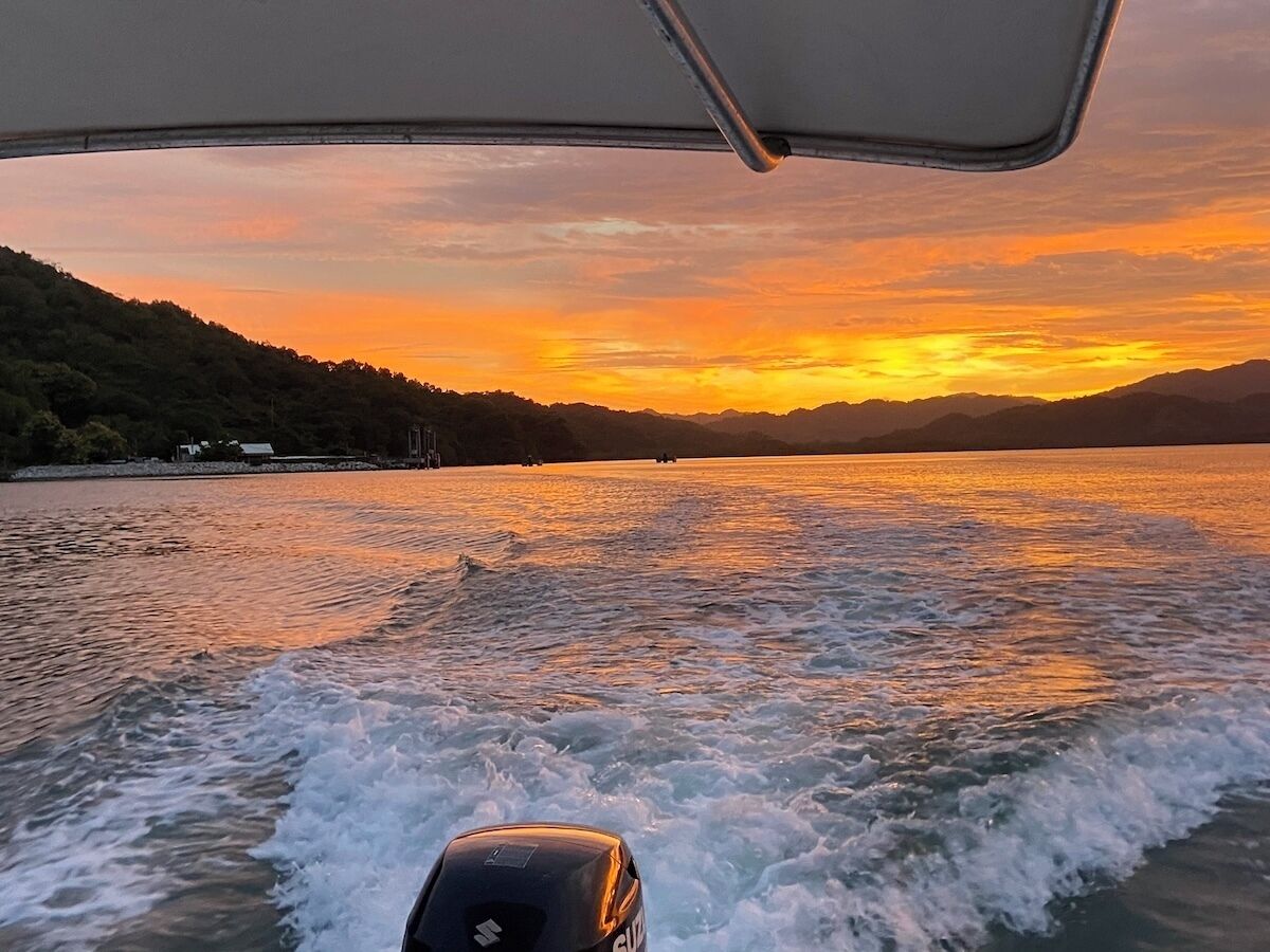Un bateau naviguant sur une étendue d’eau, avec un coucher de soleil en arrière-plan.
