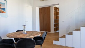 Un intérieur moderne avec une table ronde en bois, des chaises noires, une cloison en lattes de bois et un escalier.
