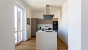 Une cuisine moderne dotée d’un îlot central, d’appareils électroménagers intégrés et de grandes fenêtres.