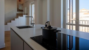 Une cuisine moderne dotée d’une plaque de cuisson à induction noire, d’une hotte en acier inoxydable et offrant une vue sur un balcon avec une balustrade.
