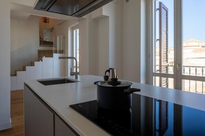 A modern kitchen with a black induction cooktop, a stainless steel range hood, and a view of a balcony with a railing. - Oretea apartment (PALERMO)