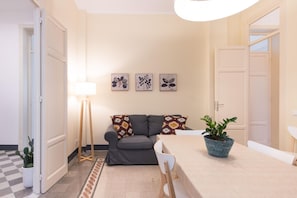 Ein Wohnzimmer mit einem grauen Sofa, einem kleinen Tisch, einer Lampe und drei Wandbildern.
