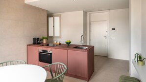 Eine moderne Küche mit einer rosa Kochinsel, einem Einbauofen und einem Spülbecken. Eine Essecke mit Stühlen und ein Blumentopf befinden sich rechts.