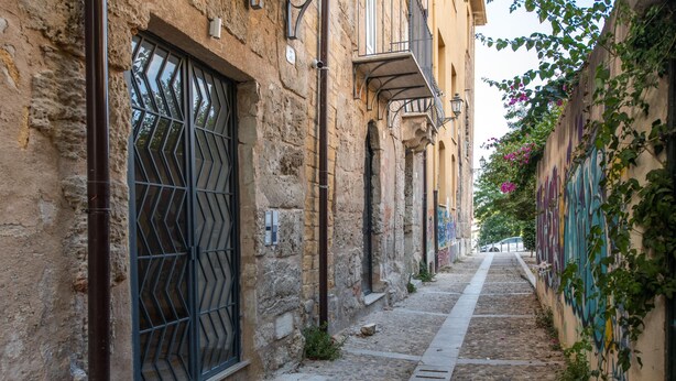 Una stretta strada acciottolata fiancheggiata da vecchi edifici in pietra con inferriate e balconi.