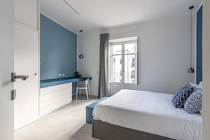 A bedroom with a bed, a desk, a chair, a window with curtains, and a view of buildings outside. - Cozy Azul suite alla Cala (PALERMO)