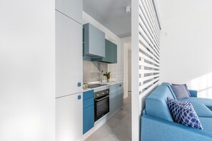 A modern kitchen with built-in appliances, a blue sofa with patterned cushions, and a white railing. - Cozy Azul suite alla Cala (PALERMO)