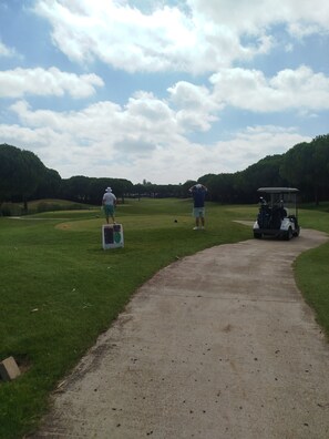 Un parcours de golf avec un chemin bien défini, un chariot de golf et deux personnes debout sur l’herbe.