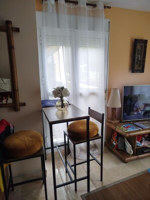 Un comedor con una mesa, sillas, un florero con flores, una lámpara y un televisor.