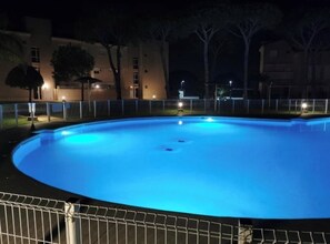 Una piscina de noche con edificios aledaños y una valla.