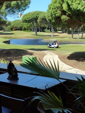 Een golfbaan met een vijver, bomen en een standbeeld.