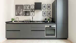 Eine moderne Küche mit grauen Schränken, einem eingebauten Ofen, einem Edelstahlkühlschrank und einem wandmontierten Gasherd.