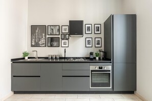 A modern kitchen with grey cabinetry, a built-in oven, a stainless steel refrigerator, and a wall-mounted gas stove. - Parlatore design apartment (PALERMO)