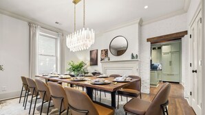Un comedor con una mesa de madera, sillas, una araña y una chimenea.