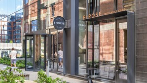 Un edificio con fachada de vidrio, un cartel que dice 'E+ROSE WELLNESS CAFE' y un área de asientos al aire libre visible.