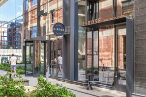 Ein Gebäude mit Glasfassade, einem Schild mit der Aufschrift 'E+ROSE WELLNESS CAFE' und einem sichtbaren Außenbereich mit Sitzgelegenheiten.