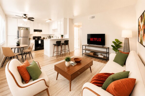 Una sala de estar moderna con sofá, sillones, una mesita de centro, televisor y una zona de cocina.