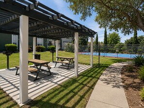 Un patio techado con mesas de picnic, una piscina y un césped bien cuidado.