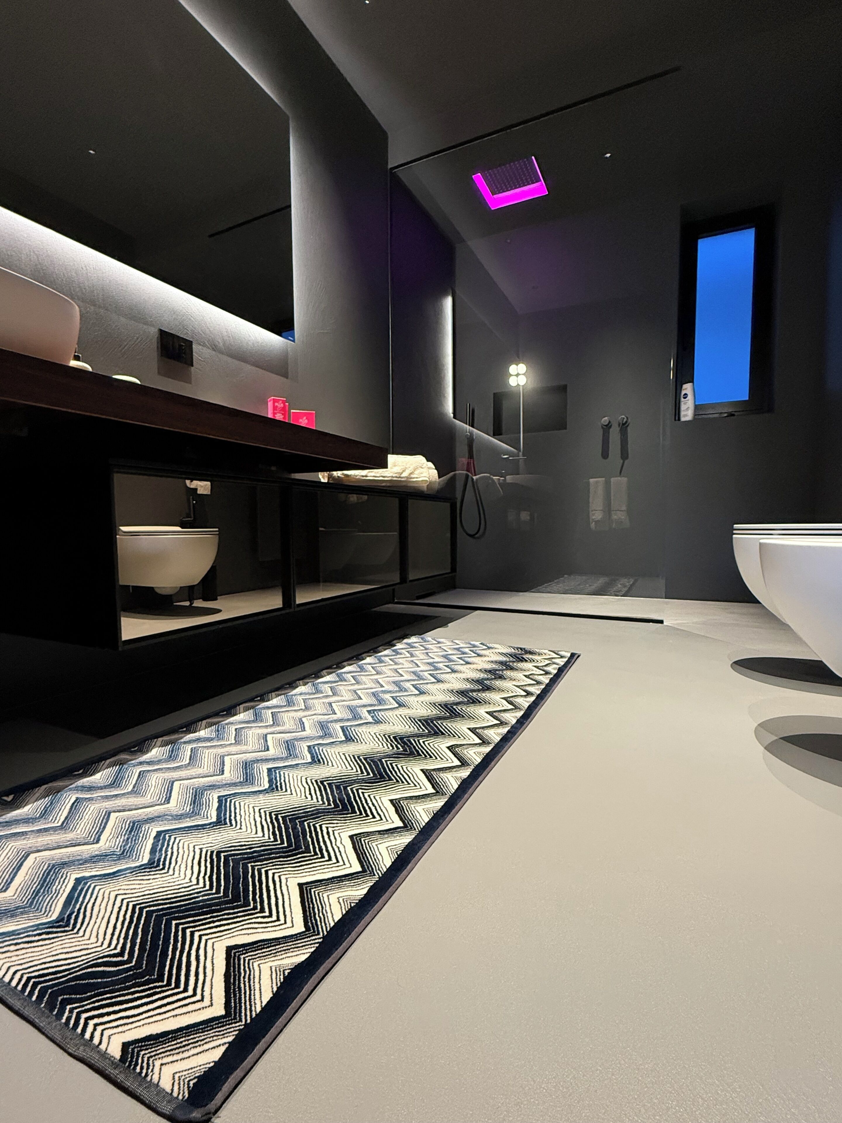 A modern bathroom with a large mirror, a bathtub, and a patterned rug.