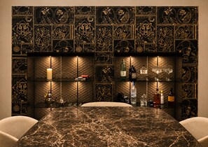 A bar area with a marble countertop, shelves with bottles, and a wall with intricate designs. - ASTRA PENTHOUSE (Bologna)