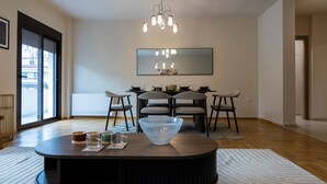 Een moderne eethoek met een ronde tafel, stoelen, een kroonluchter, een grote spiegel en uitzicht door een glazen deur.