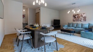 Een moderne woonkamer met een bank, een salontafel en een televisie. Er is een eethoek met een ronde tafel en stoelen.
