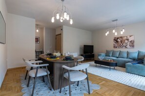 Un salon moderne avec un canapé, une table basse et un téléviseur. On y trouve également un coin repas avec une table ronde et des chaises.