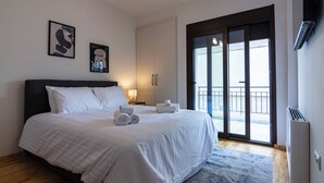 Een slaapkamer met een bed, twee kunstwerken aan de muur, een nachtkastje, een raam met uitzicht en een schuifdeur naar een balkon.