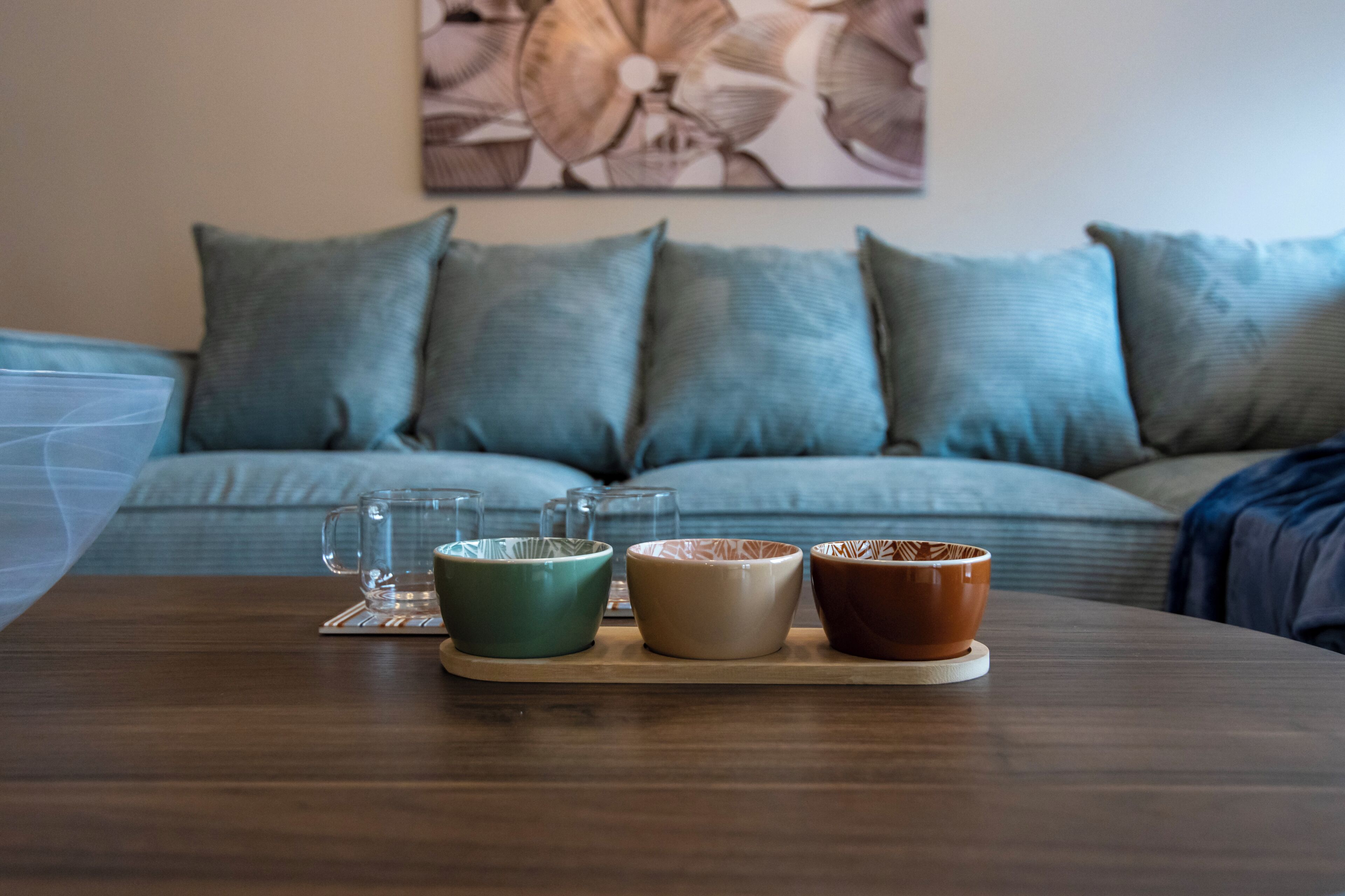 A wooden table with three ceramic bowls and a glass mug, set on a coaster.