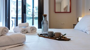 Een hotelkamer met een bed, handdoeken, een dienblad met een fles, bekers en een lepel.
