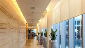 Een moderne hotelgang met marmeren wanden, grote ramen en potplanten.