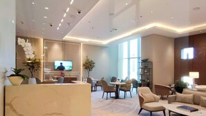 Een moderne hotellobby met een televisie, zithoek en grote ramen.