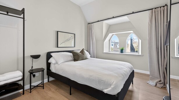 Un dormitorio moderno con cama, mesita de noche, lámpara de pie y ventana con cortinas.